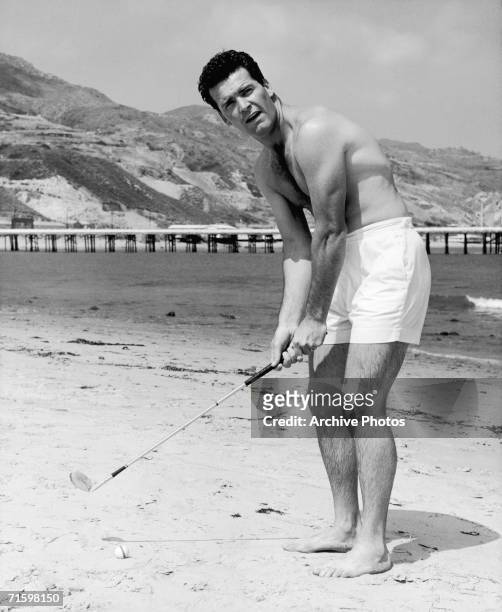 American film star James Garner practises his golf stroke on the beach in Malibu, circa 1960.