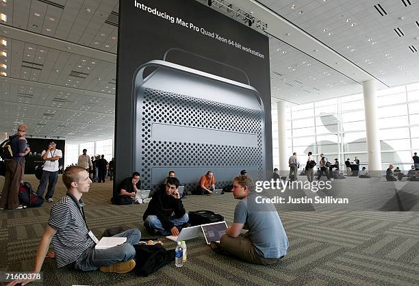 Conference attendees at the 2006 Apple Worldwide Developer's Conference work on their laptops before a poster featuring the new Apple Mac Pro desktop...