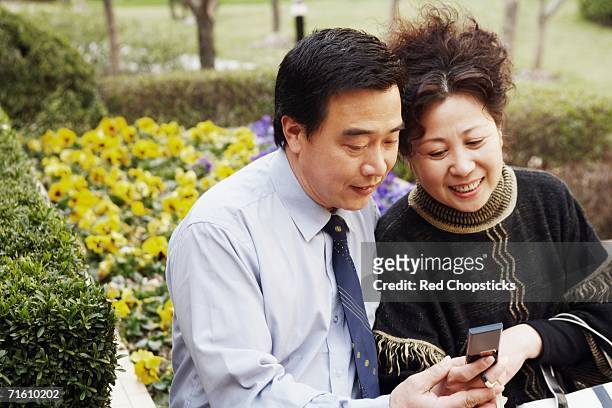 mature couple looking at a mobile phone smiling - hedge fonds stock pictures, royalty-free photos & images
