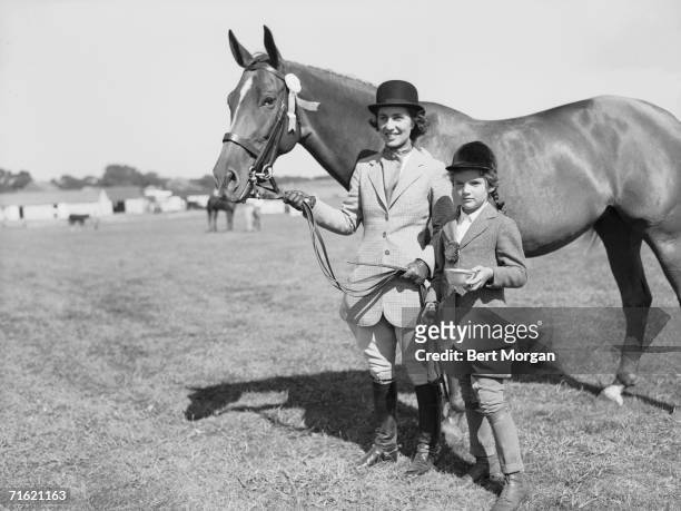 American socialite Janet Lee Bouvier and her young daughter, future first lady Jacqueline Bouvier , both dressed in riding habits, stand on a lawn...