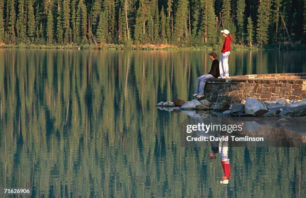 two people on wall overlooking still waters of lake louise, banff national park, canada - lake louise ストックフォトと画像