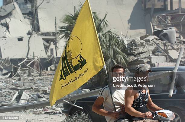 Men fly the Hezbollah flag as Lebanese, battered by five weeks of war between Israel and Hezbollah, return to the Hezbollah stronghold of Haret Hreik...
