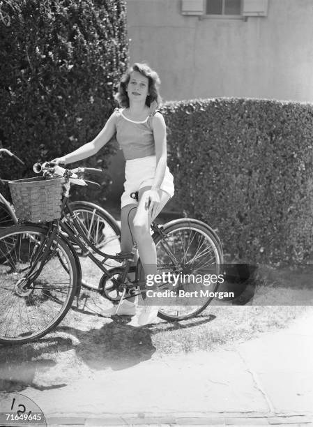 Future American fashion designer Mary McFadden sits on a bicycle by the entrance of the Southampton Bathing Corporation, Southampton, New York, mid...