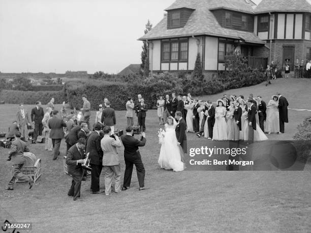 American socialite Anne McDonnell Ford and her new husband automobile executive Henry Ford II pose before a large group of movie and still...