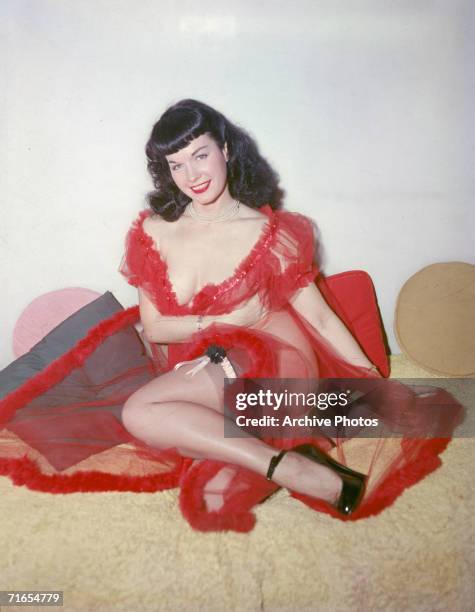 American glamour model and pin-up girl Bettie Page poses in a red negligee and stockings, circa 1955.