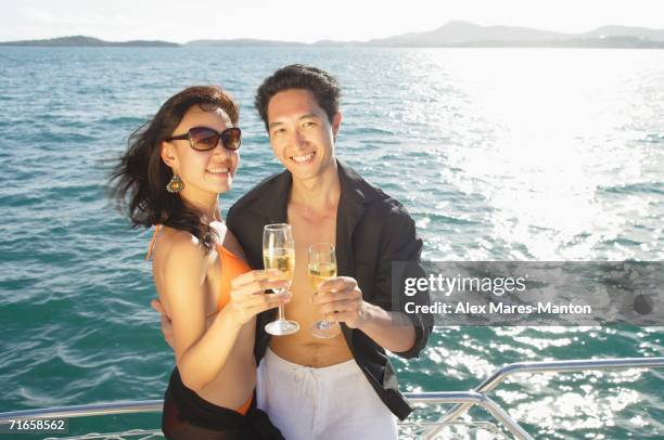 couple on boat deck, standing next to railing, holding champagne glasses, smiling at camera - holding on to railing stock pictures, royalty-free photos & images