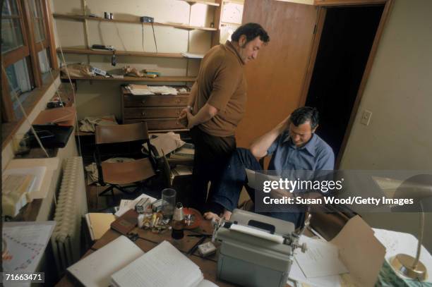 American authors and hoax perpetrators Clifford Irving and Richard Suskind work inside a messy office, 1972. Irving sits at a desk with his bare foot...