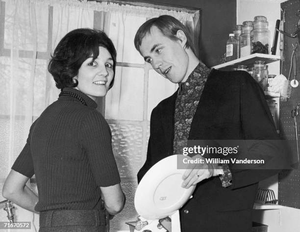 British disc jockey and entertainer Simon Dee helps his wife, Bunny, with the washing up at their home in Finchley, north London, 15th December 1966.