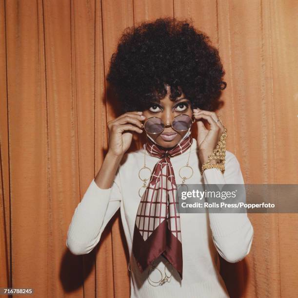 American singer and lead singer of The Supremes, Diana Ross pictured wearing a neck scarf and holding a pair of metal rimmed sunglasses in London in...