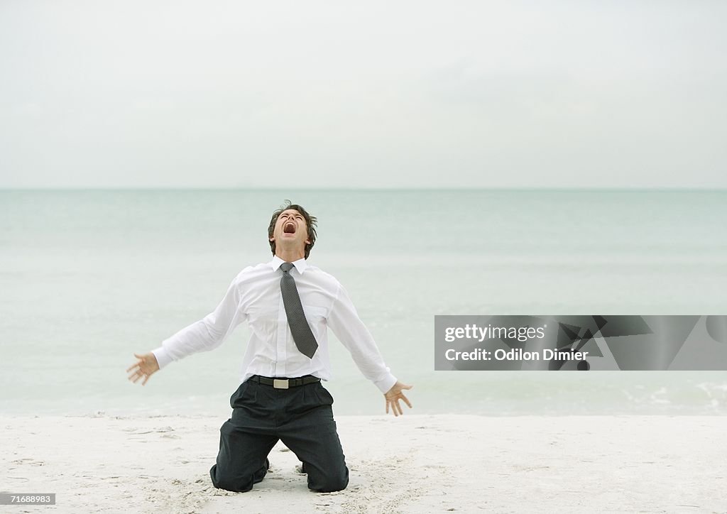 Businessman down on knees, screaming, on beach