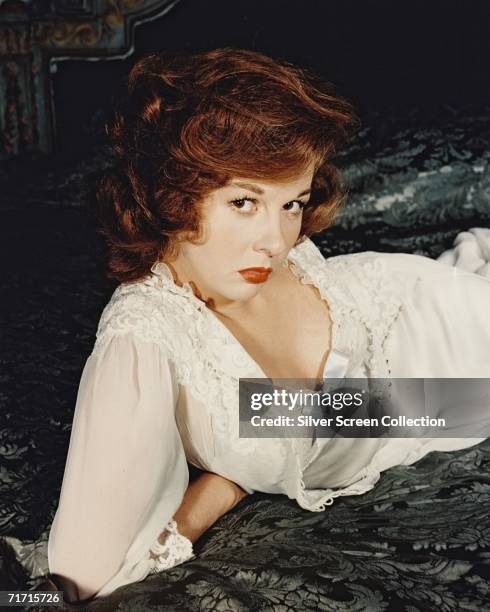 American actress Susan Hayward reclines on a bed in a white lace negligee, circa 1950.