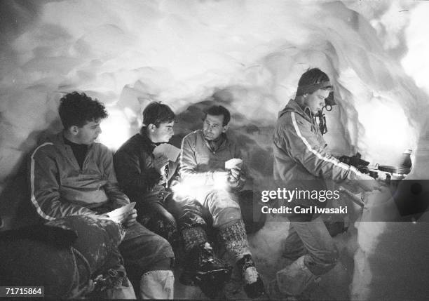 Two Air Force Academy cadets play cards with their instructor in a snow cave while a third cadet cooks over a camp stove on a ledge in the cave, near...