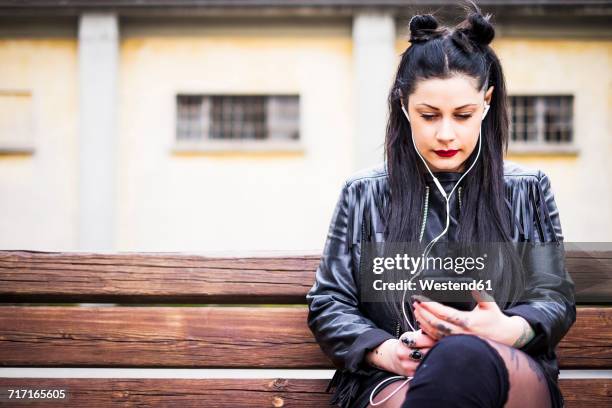 dark-haired young woman sitting on bench listening music with earphones and smartphone - women wearing black stockings stock pictures, royalty-free photos & images