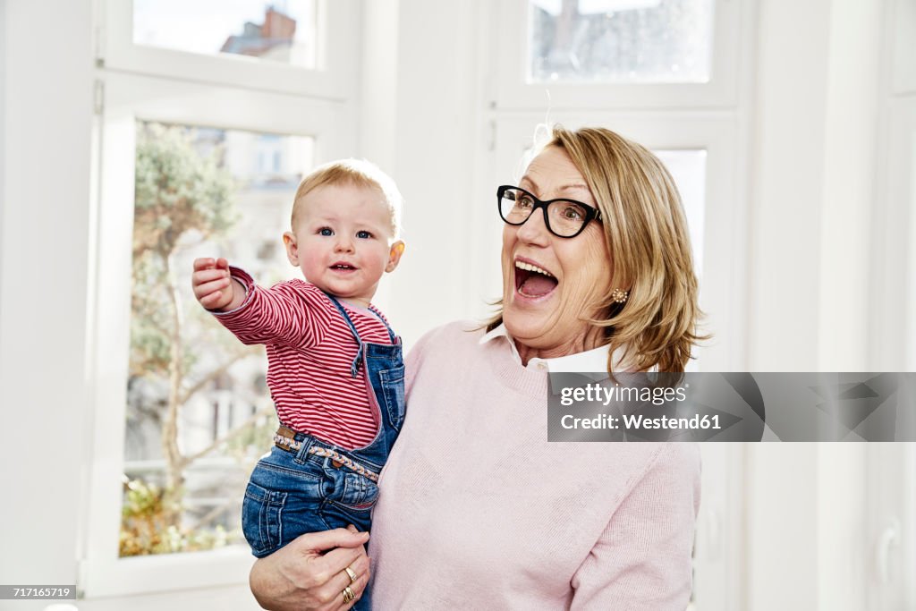 Happy grandmother carrying baby girl at home