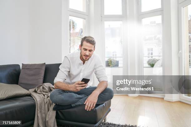 man sitting on couch looking at cell phone - 胡坐　横 ストックフォトと画像