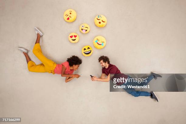 happy couple texting on their smart phones, sending emojies - smiley stockfoto's en -beelden