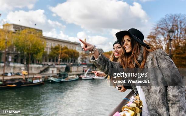 france, paris, two young women leaning on a bridge over the seine river - paris millenials stock-fotos und bilder