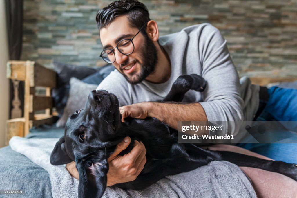 Smiling man stroking his dog on the couch at home