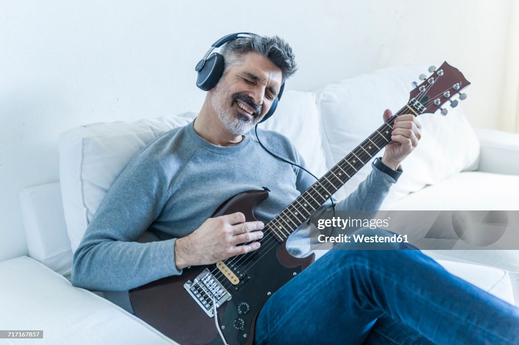 Mature man at home playing electric guitar and wearing headphones