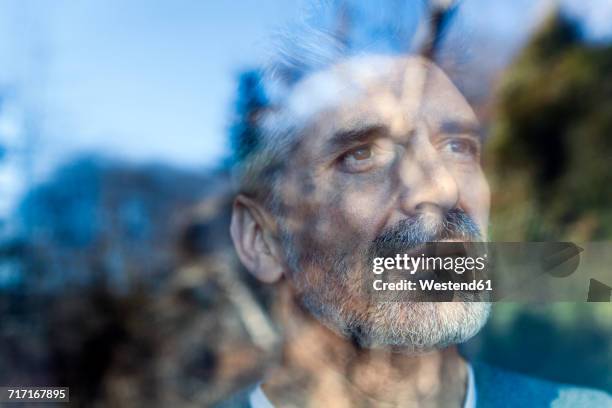 mature man looking out of window - spiegelung scheibe stock-fotos und bilder