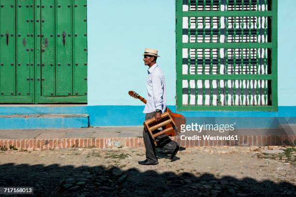 cuba, trinidad, walking man with guitar and stool on the street - caribbean musical instrument stock pictures, royalty-free photos & images
