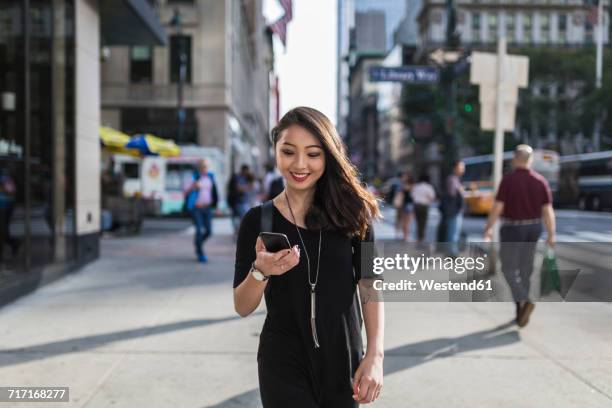 usa, new york city, manhattan, portrait of smiling young woman dressed in black looking at cell phone - sidewalk fotografías e imágenes de stock