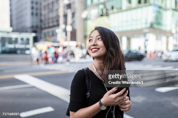 usa, new york city, manhattan, young woman listening music with cell phone and earphones on the street - asian tourist bildbanksfoton och bilder