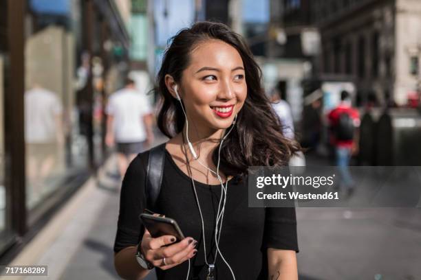 usa, new york city, manhattan, young woman listening music with cell phone and earphones on the street - music city walk stock pictures, royalty-free photos & images