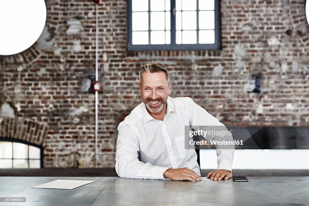 Portrait of happy businessman sitting at table in a loft