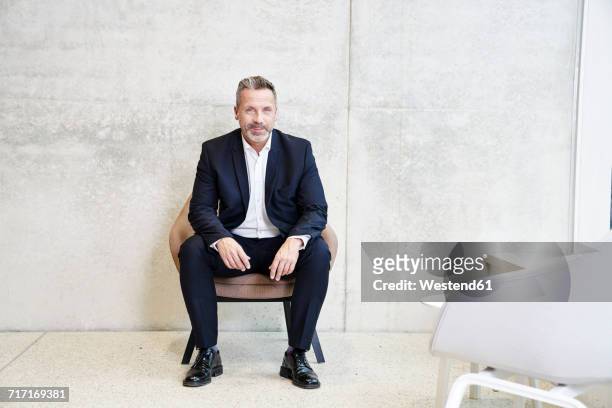 portrait of smiling businesssman sitting in armchair - sitzen stock-fotos und bilder