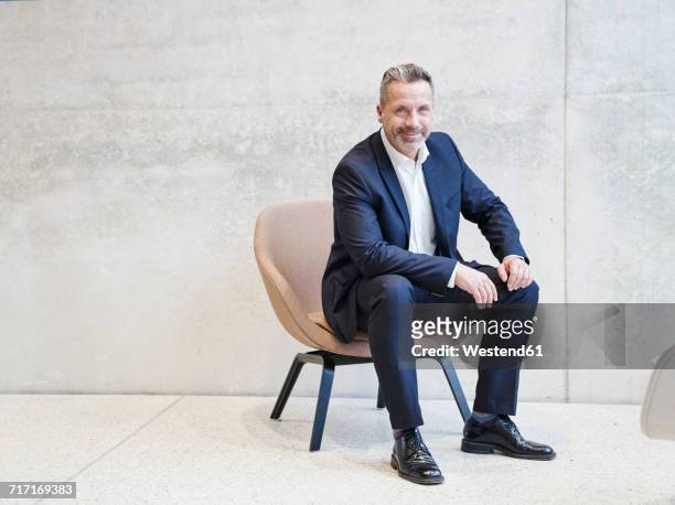 portrait of smiling businesssman sitting in armchair - sitzen stock-fotos und bilder
