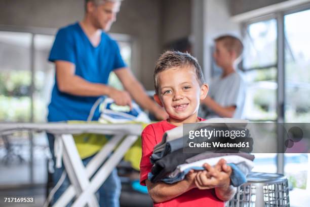 smiling boy helping with chores holding folded clothes - laundry africa stock pictures, royalty-free photos & images