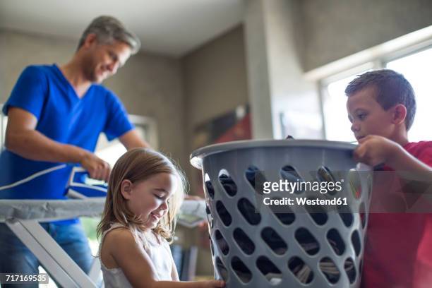 two children helping father with chores carrying laundry basket - man washing basket child stock pictures, royalty-free photos & images