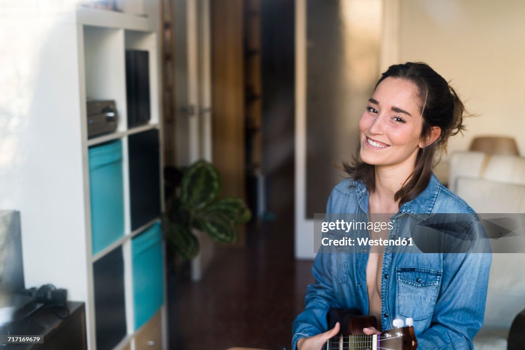 Smiling young woman playing ukulele at home