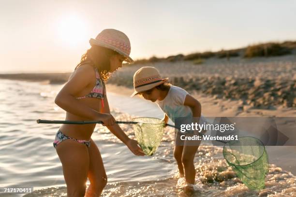 spain, menorca, two girls with dip nets on the beach - fresh fish stockfoto's en -beelden