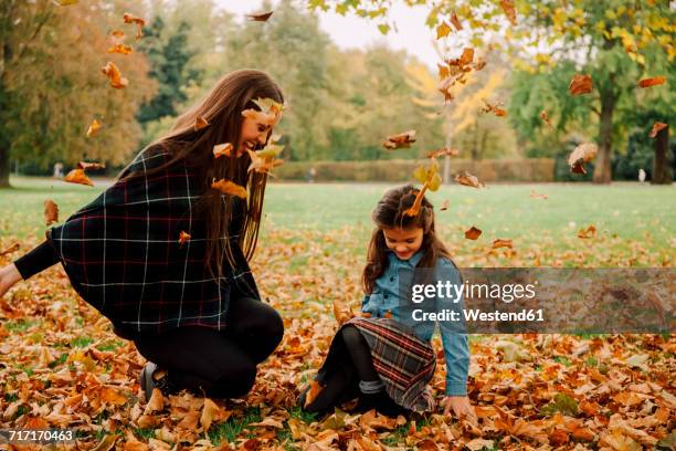 young woman and little girl playing with autumn leaves on a meadow - fashionable family stock pictures, royalty-free photos & images