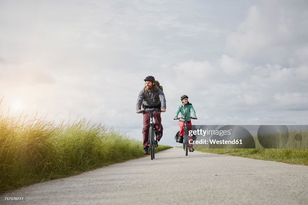 Germany, Schleswig-Holstein, Eiderstedt, couple riding bicycle on path through salt marsh