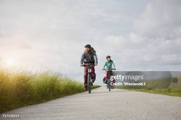 germany, schleswig-holstein, eiderstedt, couple riding bicycle on path through salt marsh - tidal marsh stock pictures, royalty-free photos & images