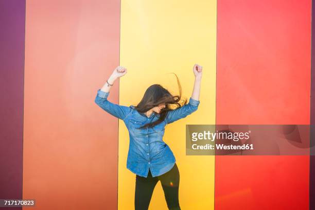 happy young woman dancing in front of colourful wall - solo una donna giovane foto e immagini stock