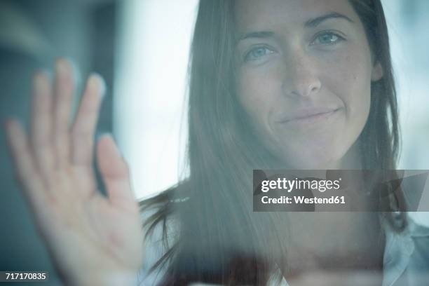 portrait of smiling young woman behind windowpane - waving goodbye stock pictures, royalty-free photos & images