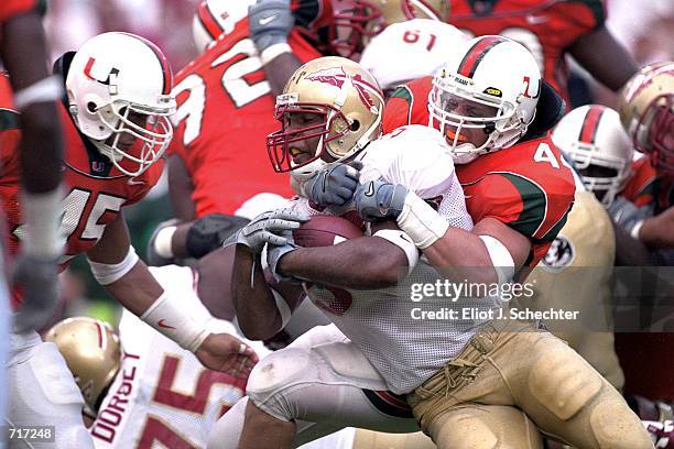 William McCray of the Florida State Seminoles gets pulled down with the ball by Howard Clark and Dan Inongaw of the Miami Hurricanes during the game...