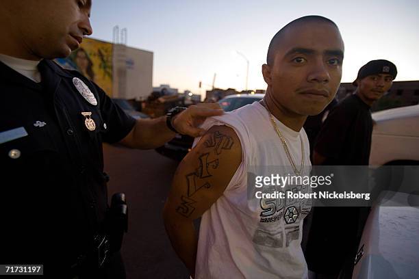 With three 18th Street gang members detained, a Los Angeles gang police officer checks a tattoo of a member on August 4, 2006 in the Rampart area in...