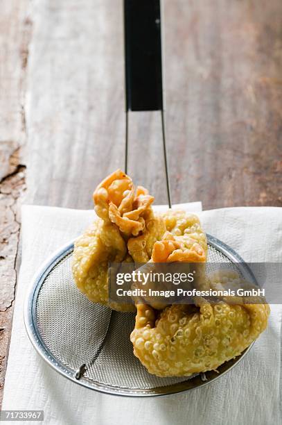 two deep-fried wontons on straining spoon - schuimspatel stockfoto's en -beelden