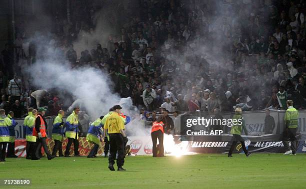 Members of the staff's stadium rush to the pitch after flares were thrown onto the pitch during the derby soccer match between Swedish Cup teams...