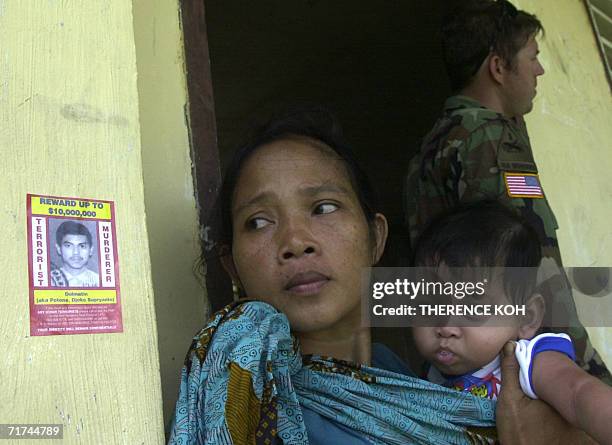 Woman waits outside a school building used as a clinic beside a card bearing the portrait of wanted Indonesian terror suspect Dulmatin29 August 2006...