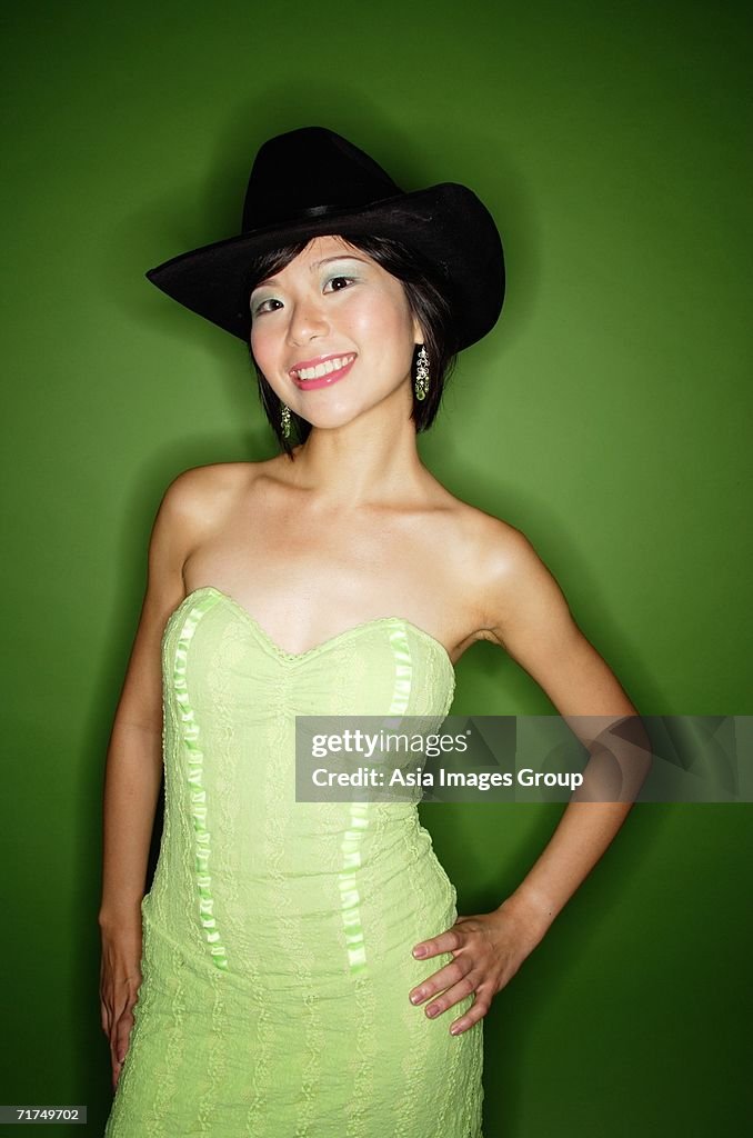 Woman in green dress, wearing cowboy hat and earrings, smiling at camera