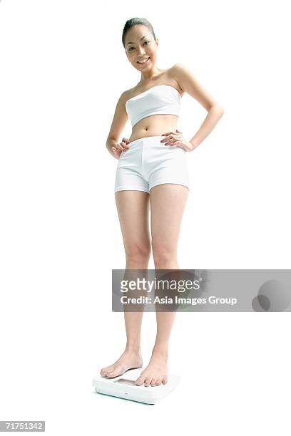 young woman standing on weighing scale, hands on hips, smiling at camera - strapless stock pictures, royalty-free photos & images