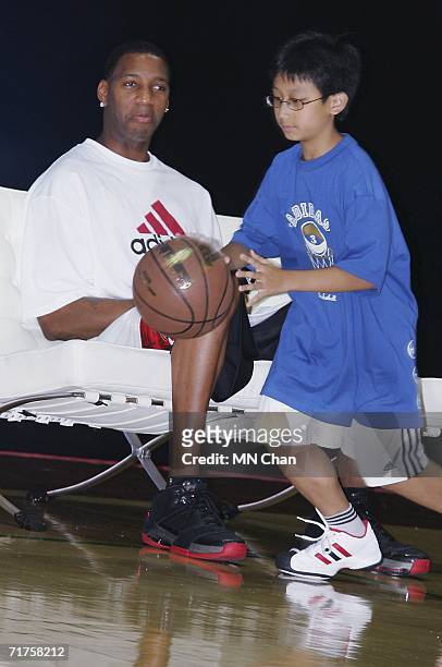 Player Tracy McGrady of the Houston Rockets watches a junior basketball player demonstrating his skill during a ceremony to launch an Adidas shoe at...