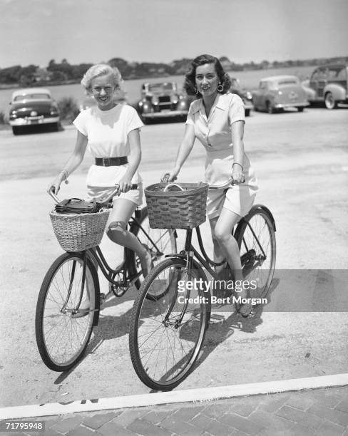 American socialites, fashion figures, and sisters Catherine Murray McManus and Jeanne Murray Vanderbilt, ride their bikes to the entrance of the...