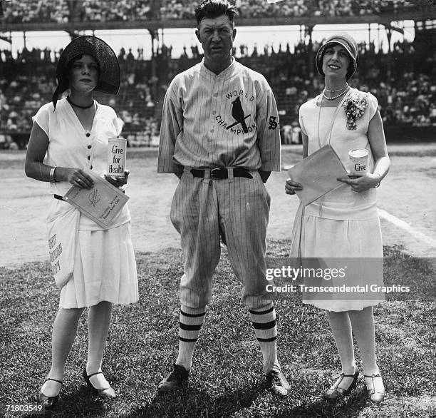 Cardinals pitcher Grover Cleveland Alexander poses before a game in Sportsmans Park in St. Louis, flanked by two flappers promoting a health charity.